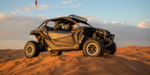 Powerful Can-Am Maverick X3 self-drive dune buggy parked on red sand dune crest in Lahbab Desert Dubai during golden hour