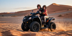 Happy couple riding a 2-seater quad bike through the Big Red dunes in Al Badayer Desert Dubai during golden sunset hour
