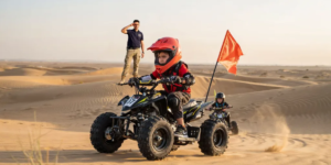 Young child riding a 50cc entry-level quad bike on a controlled practice track in the Dubai desert with safety helmet and protective gear