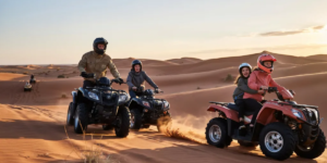 Family riding quad bikes together through the red sand dunes of the Lahbab Desert in Dubai during golden sunset hour