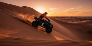 Powerful quad bike conquering the iconic Big Red dune in Al Badayer Desert at sunset with sand spraying from wheels during exhilarating self-drive adventure