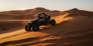 Polaris RS1 single-seater dune buggy climbing a red sand dune in Lahbab Desert Dubai during golden hour with dramatic sand spray
